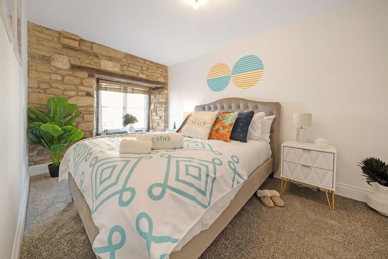 Modern bedroom with double bed, patterned bedding, wooden feature wall and potted plant