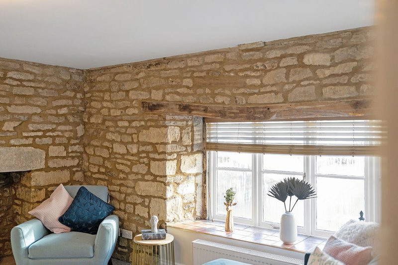 Living room corner with stone walls, armchair, window with blinds and decorative plants