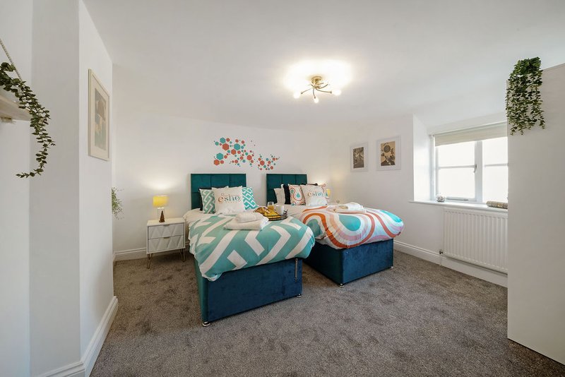 Bright bedroom with two single beds, teal headboard, geometric bedding, and potted plants