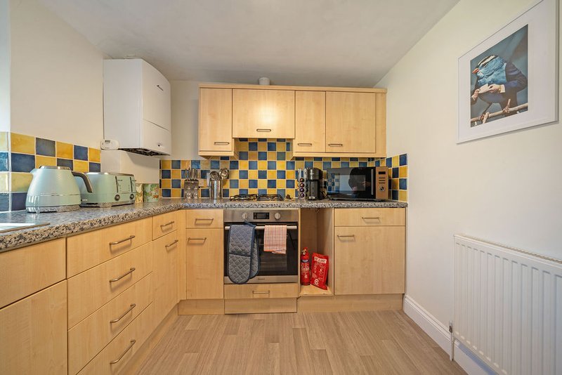Compact kitchen with wooden cabinets, blue and yellow tile backsplash, and integrated appliances