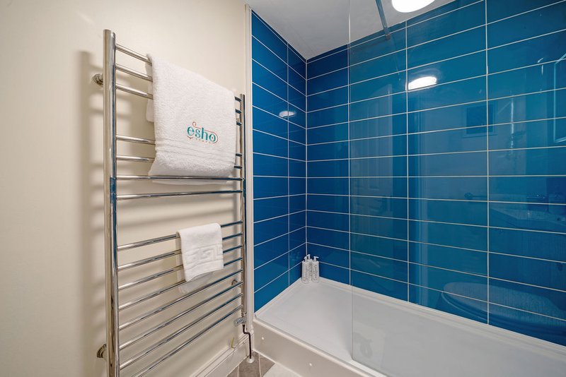 Modern bathroom with blue tile walls, white bath, heated towel rail and towels