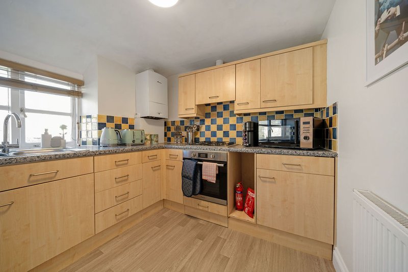 Modern kitchen with wooden cabinets, blue and black tiled backsplash, integrated appliances and window
