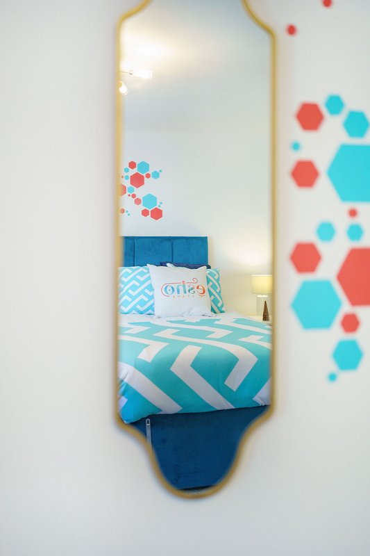 Bedroom reflected in tall gold-framed mirror with colorful geometric wall decals