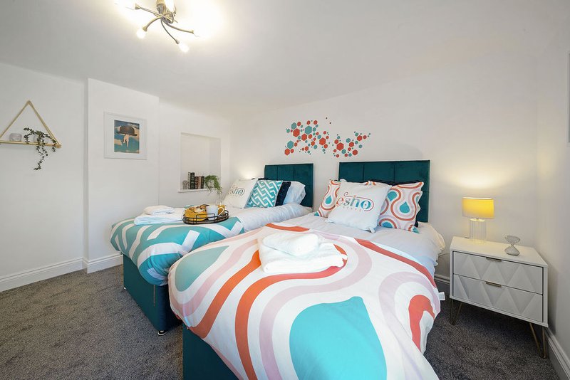Bright bedroom with two single beds, teal headboards, colorful bedding, and modern decor