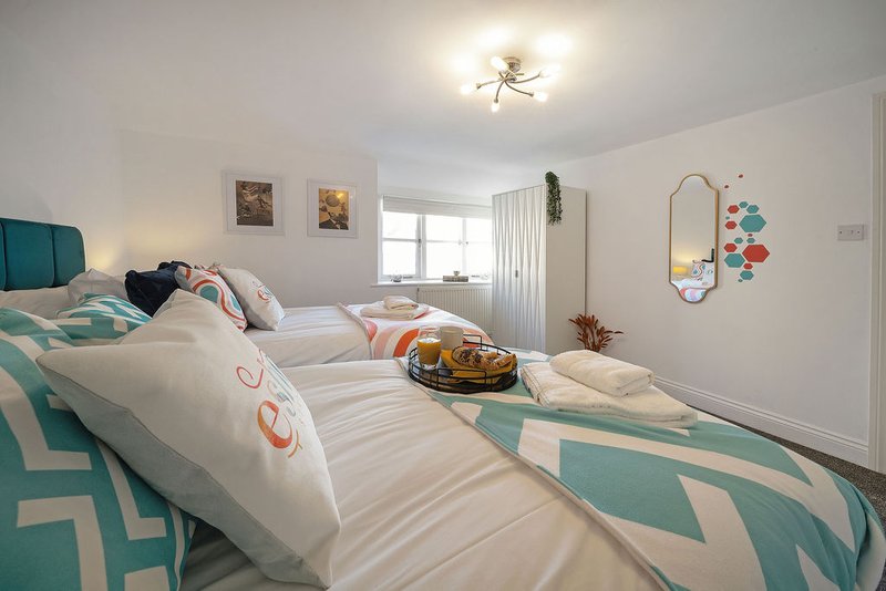 Bright modern bedroom with twin beds, teal geometric bedding, mirror, and window with curtains