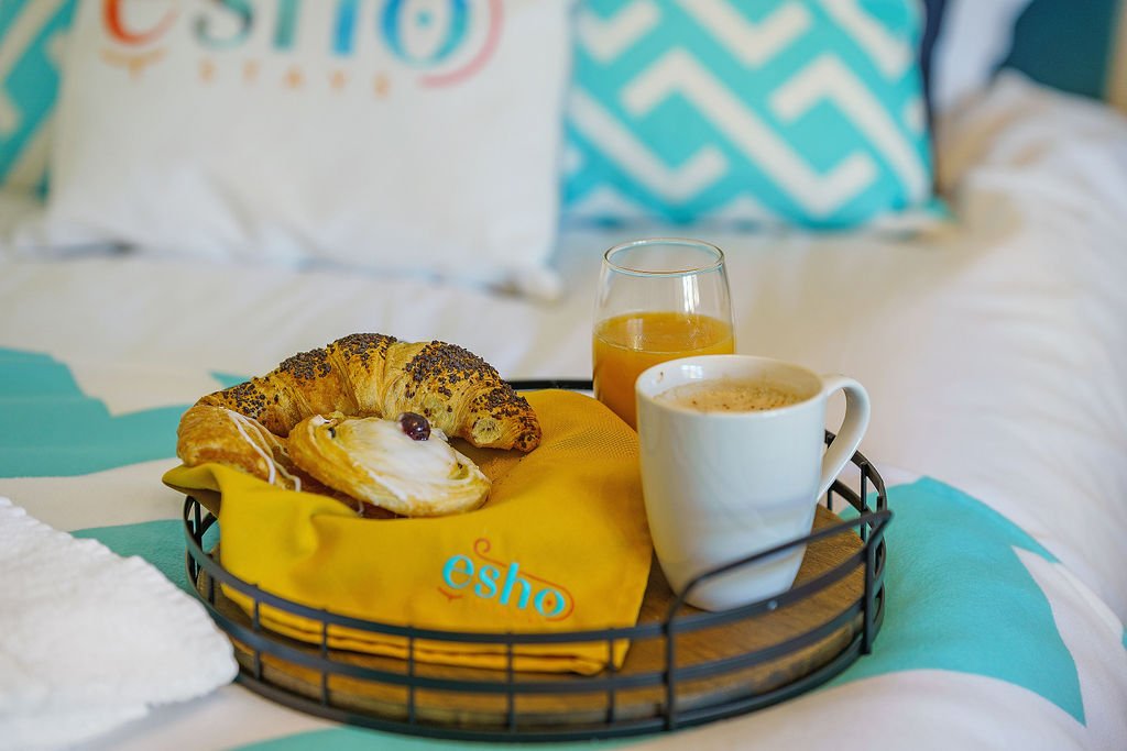 Breakfast tray with pastry, coffee cup, juice glass and decorative pillows on bed