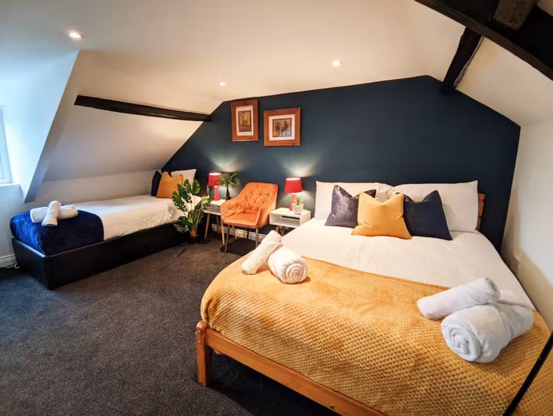 Bright attic bedroom with two beds, navy feature wall, orange accents and framed wall art