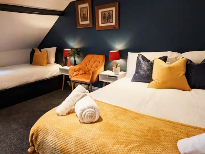 Modern bedroom with two beds, yellow bedding, dark walls, and colorful cushions and lamps