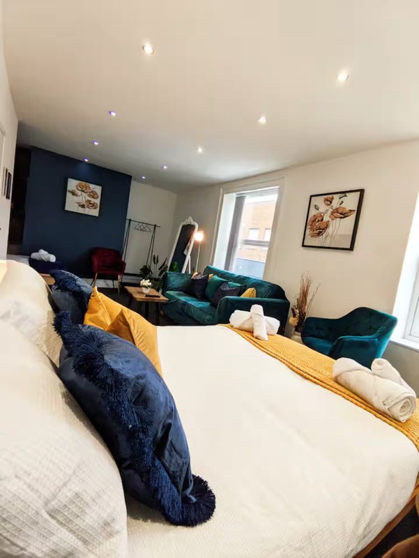 Modern bedroom with double bed, dark blue feature wall, teal velvet seating, and natural light from window