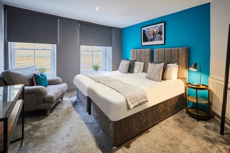 Modern bedroom with double bed, turquoise accent wall, seating area and large windows