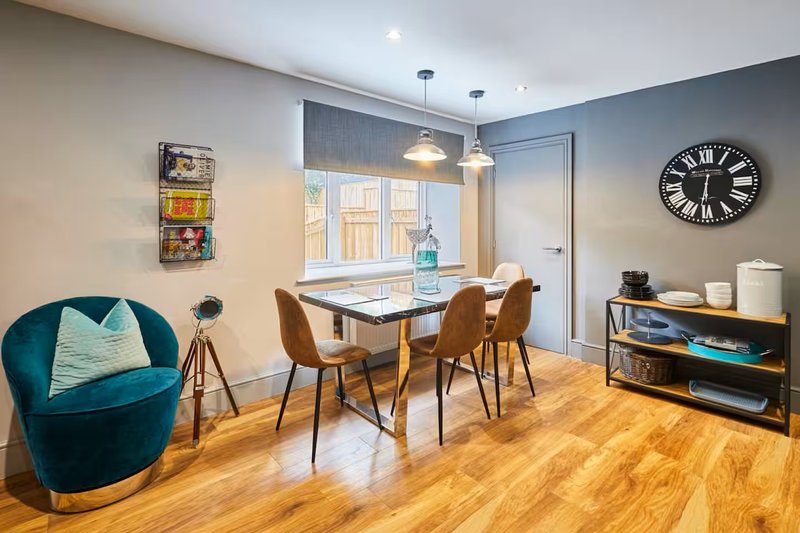 Open-plan dining and living area with wooden table, teal armchair, hardwood flooring and large windows