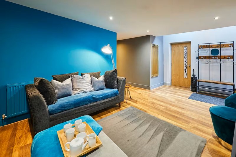 Modern living room with blue accent wall, grey sofa, wooden flooring and contemporary furnishings