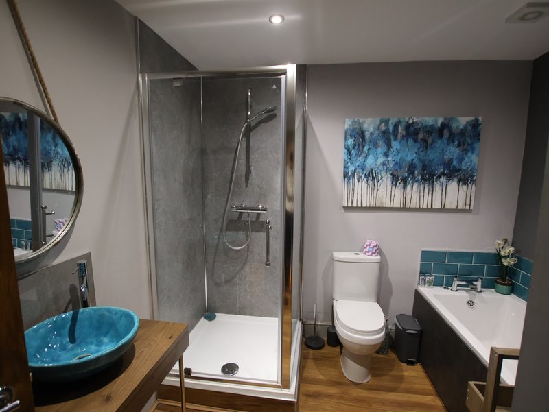 Modern bathroom with walk-in shower, blue vessel sink, toilet, and teal tile accents