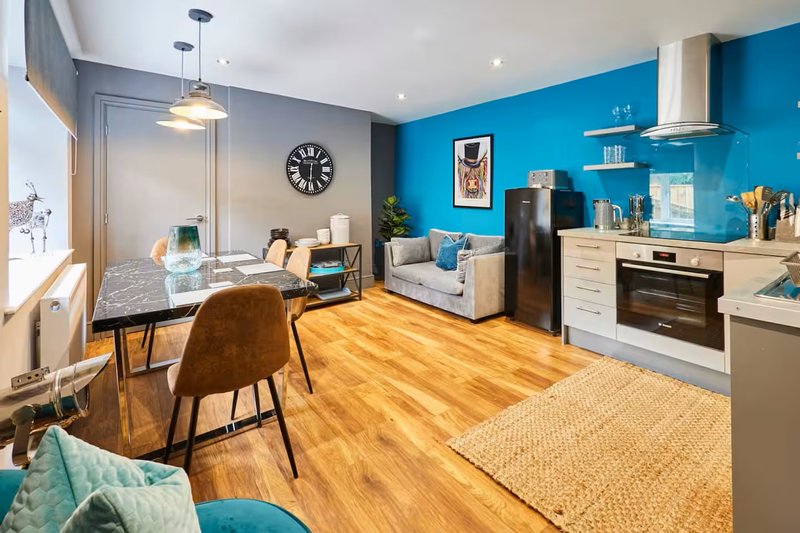 Open-plan kitchen and living area with blue accent wall, wooden flooring, and modern furnishings