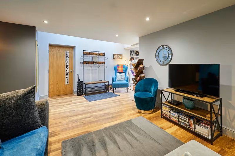 Modern living room with wooden flooring, blue armchair, TV, shelving and wall clock