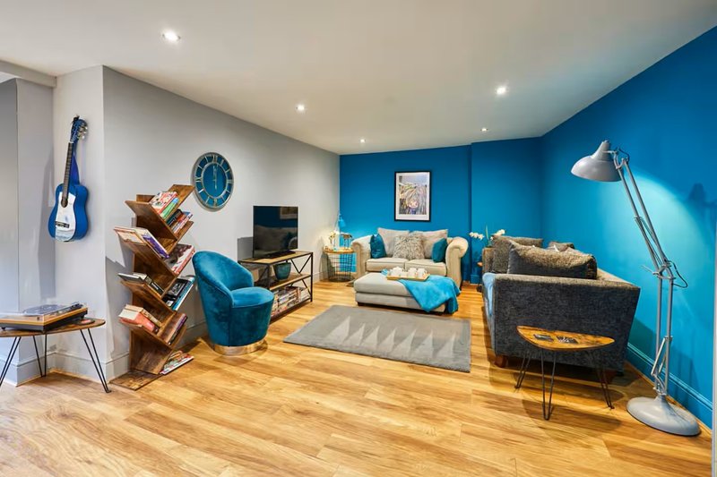 Modern living room with blue accent wall, wooden flooring, upholstered seating, and decorative guitar