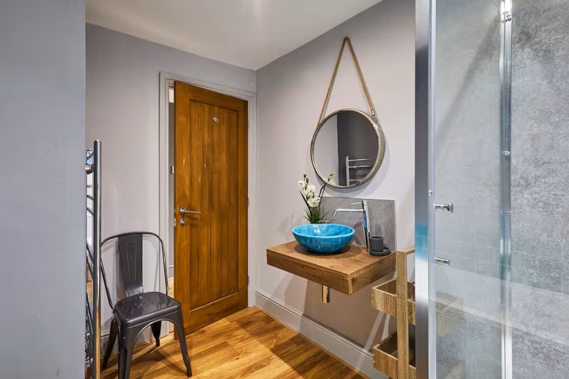 Hallway with wooden door, round mirror, wooden shelf, blue bowl and black chair