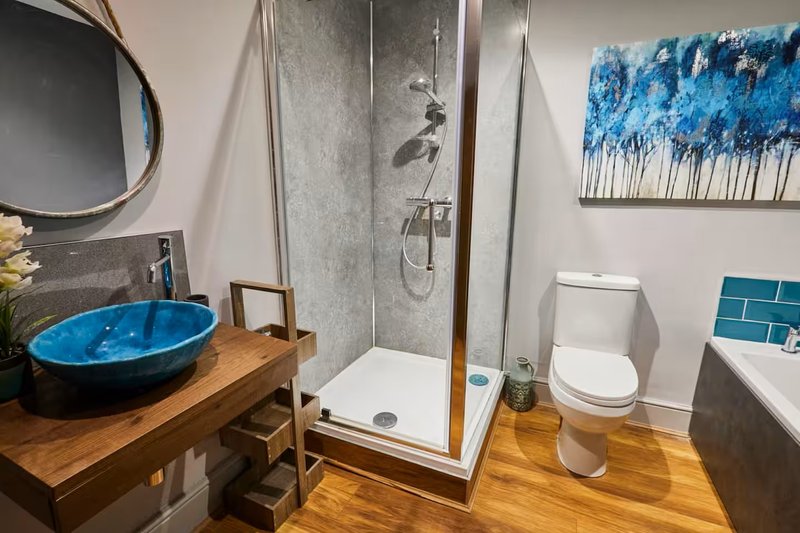 Modern bathroom with blue vessel sink, walk-in shower, toilet, and wooden flooring