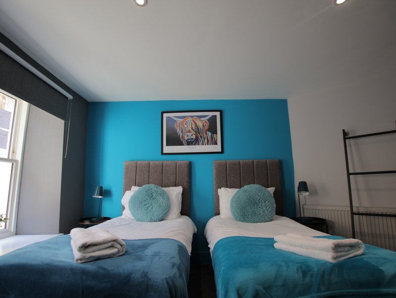 Twin bedroom with turquoise accent wall, grey headboards, white bedding and round cushions