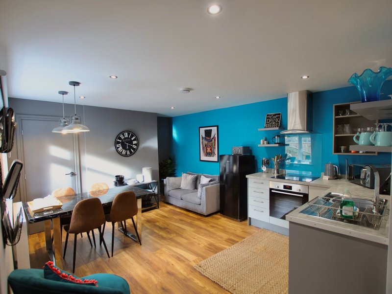 Open-plan living space with bright blue accent wall, dining table, sofa, kitchen area and wooden flooring