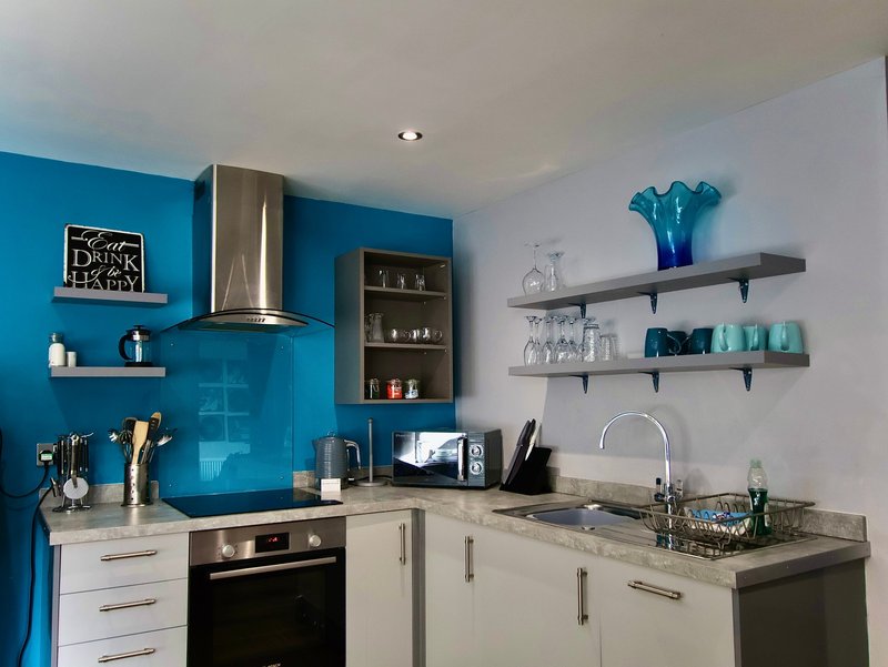 Modern kitchen with blue splashback, white cabinetry, stainless steel hood, and open shelving
