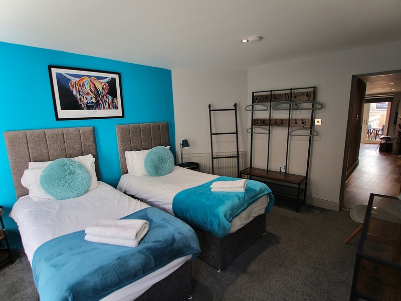 Bright bedroom with two single beds, turquoise accents, grey headboards and modern storage shelving