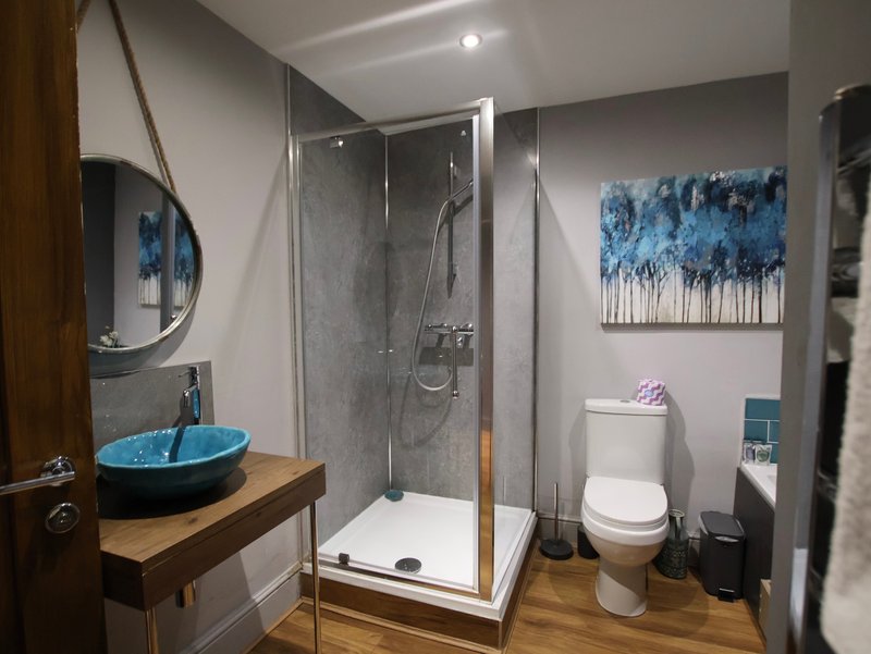 Modern bathroom with walk-in shower, blue sink, wooden vanity and toilet