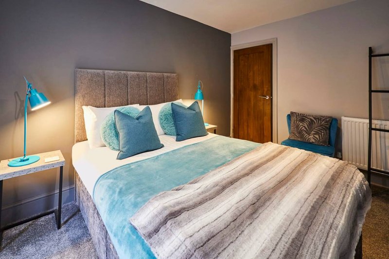 Modern bedroom with double bed, blue bedding, teal desk lamp and wooden door
