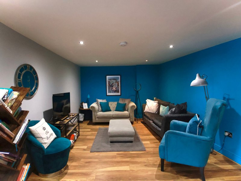 Modern living room with blue accent wall, cream and blue sofas, wooden flooring and pendant lighting
