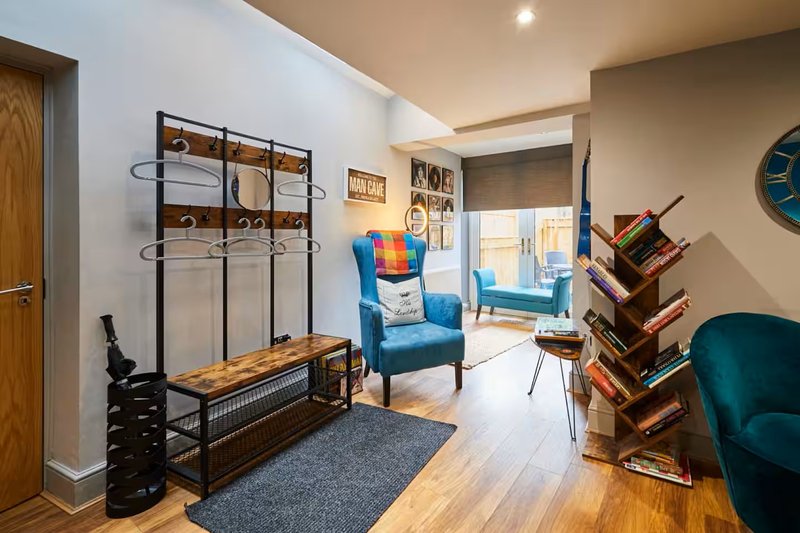Modern living room with blue armchair, wooden shelving, coat rack, and hardwood flooring