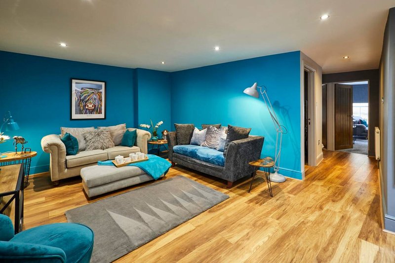 Modern living room with turquoise walls, cream and teal upholstered seating, wooden flooring and contemporary lighting.