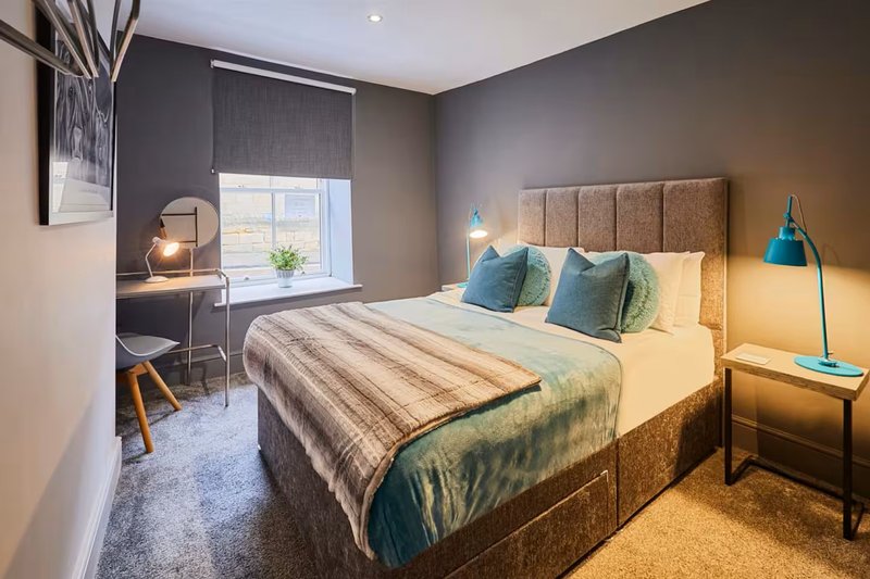 Modern bedroom with double bed, teal cushions, desk, floor lamp and window view