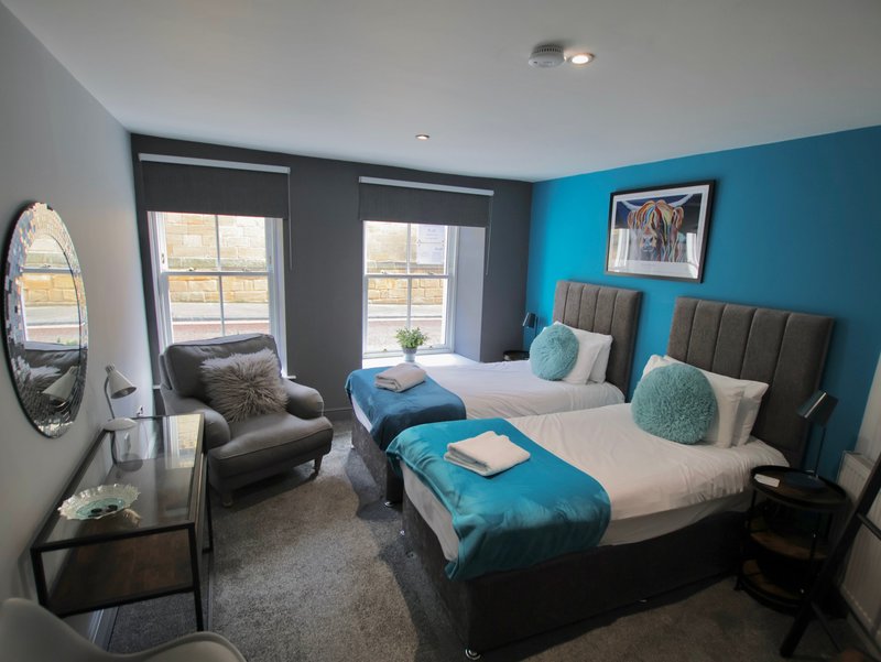 Modern twin bedroom with teal accent wall, two beds, grey upholstered headboards and glass doors