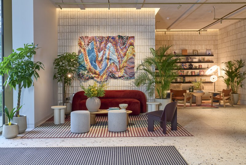 Modern lobby interior with burgundy sofa, potted plants, abstract artwork and contemporary furnishings