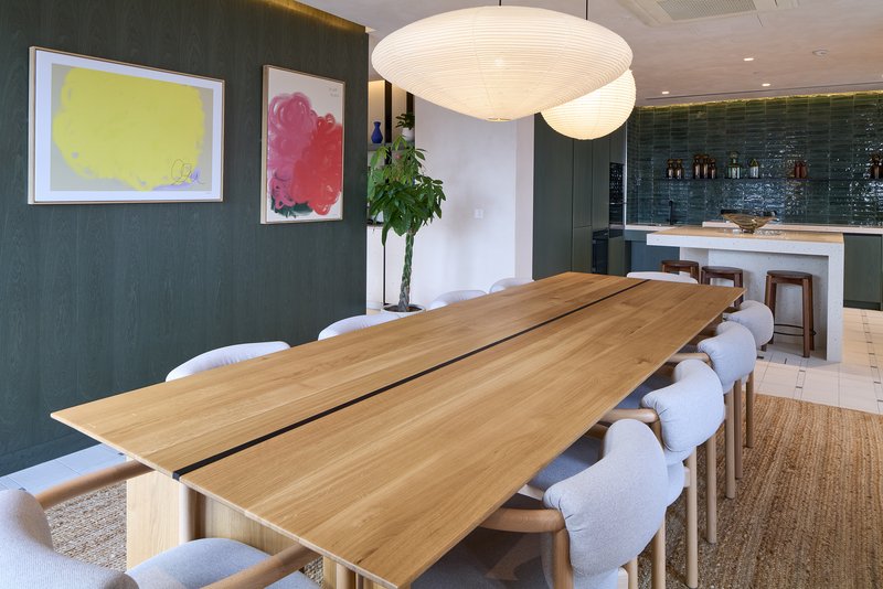 Modern dining room with wooden table, upholstered chairs, pendant lighting and kitchen visible