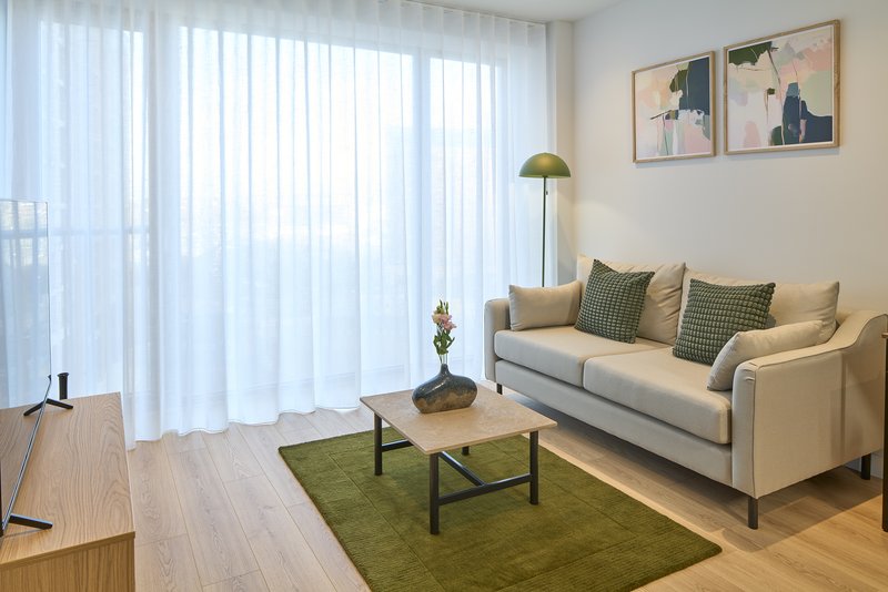 Bright living room with cream sofa, wooden coffee table, green rug and floor-to-ceiling windows