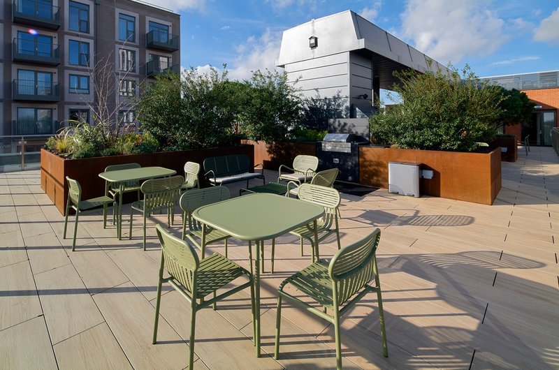 Communal rooftop terrace with green tables, chairs, planters and city views