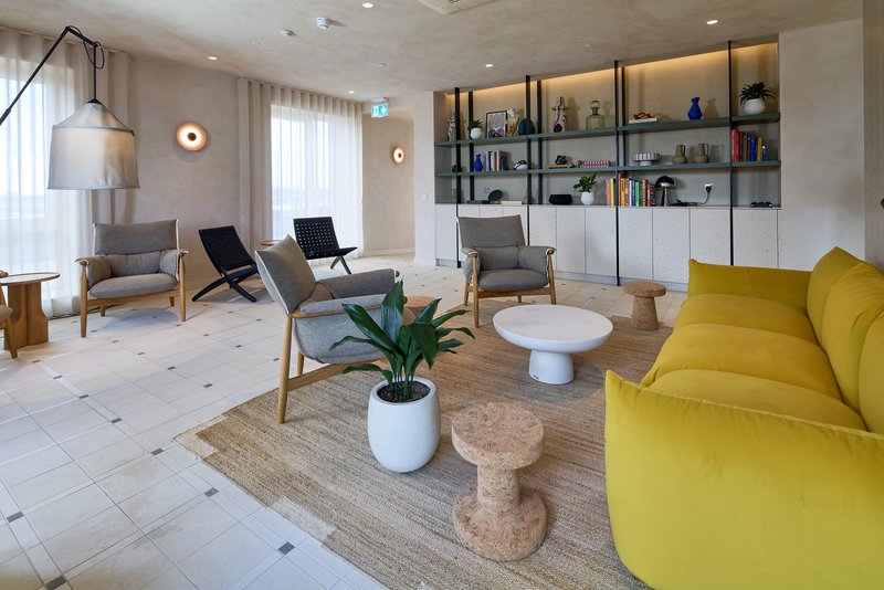 Modern living room with yellow sofa, chairs, shelving unit, potted plant and round coffee table