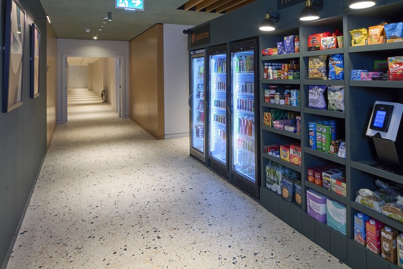 Modern corridor with polished concrete floor, refrigerated display cases, shelving with packaged goods, and wood-paneled doorway
