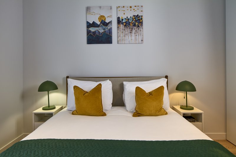 Modern bedroom with double bed, yellow cushions, green bedside lamps and wall art
