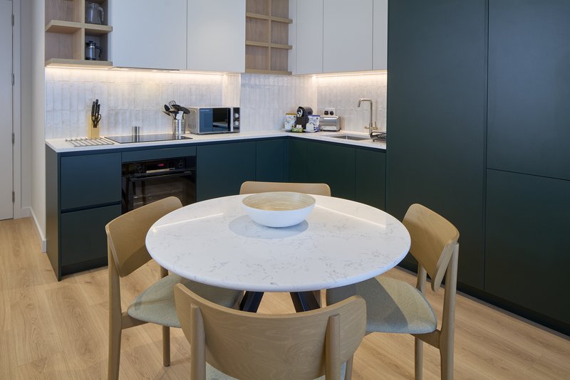 Modern kitchen and dining area with round white table, wooden chairs, dark cabinetry and pendant lighting