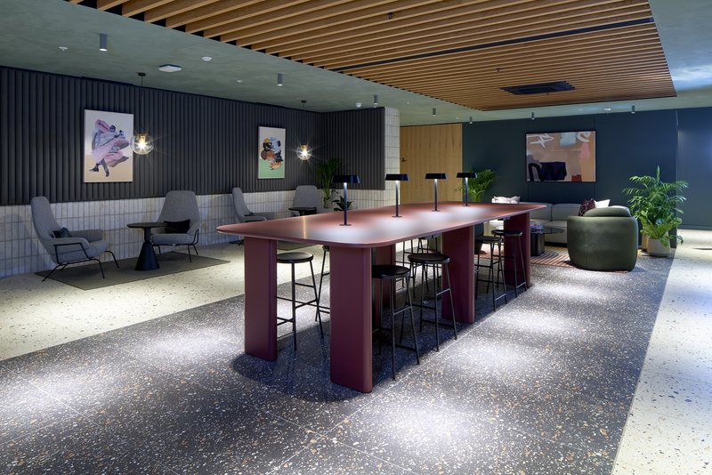 Modern open-plan communal space with burgundy kitchen island, grey seating, and wooden ceiling