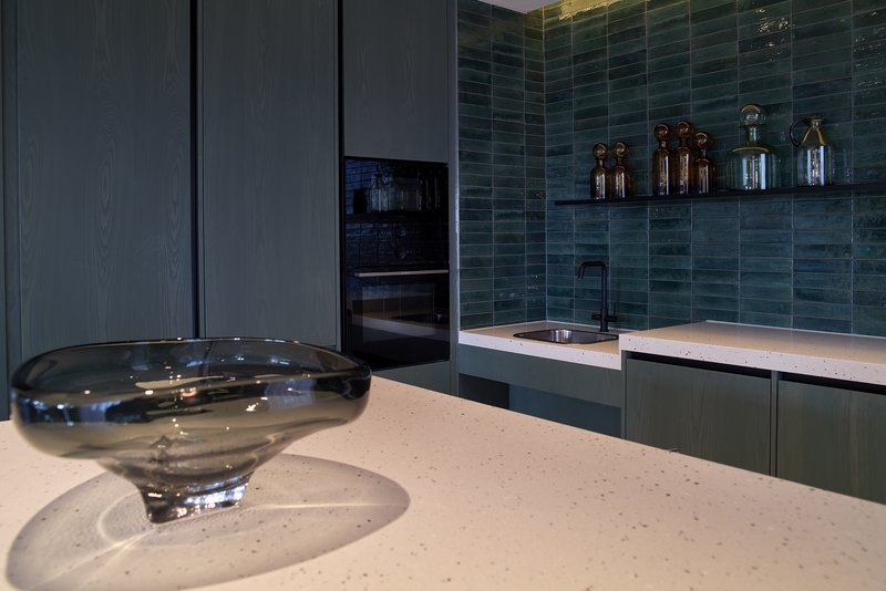 Modern kitchen with teal tile backsplash, white countertop, built-in oven and decorative glass bowl