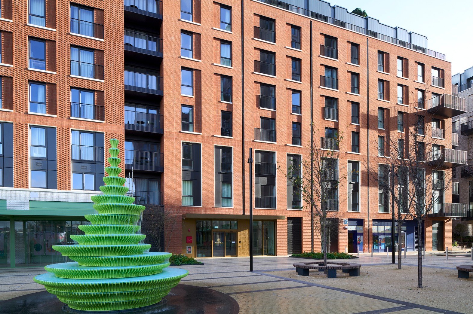 Modern brick apartment building with green courtyard sculpture and seating areas