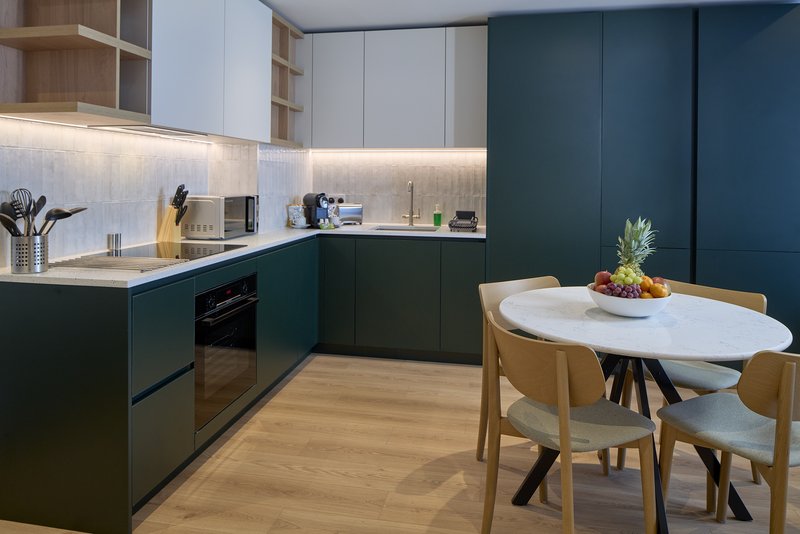 Modern kitchen with dark teal cabinetry, white countertops, dining table with wooden chairs
