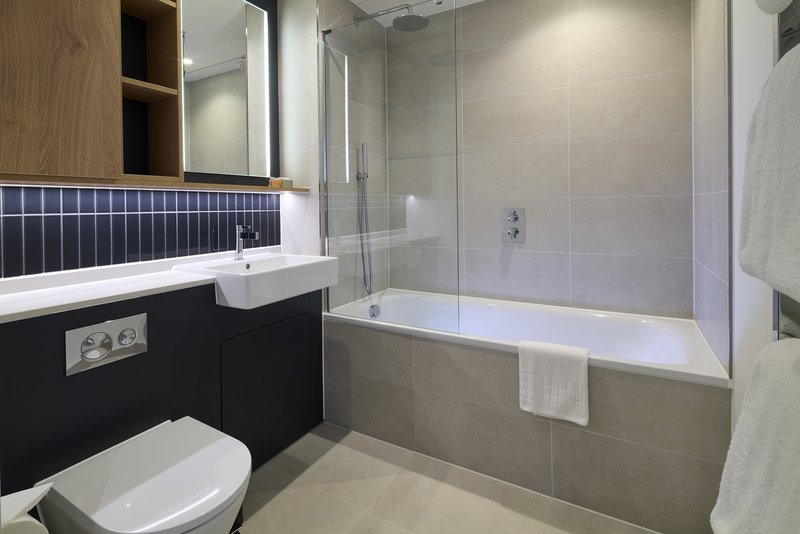 Modern bathroom with white sink, black vanity, toilet, bathtub with glass screen and towel rail