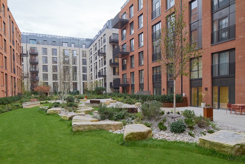 Modern brick apartment building courtyard with manicured lawn, stone seating areas and young trees