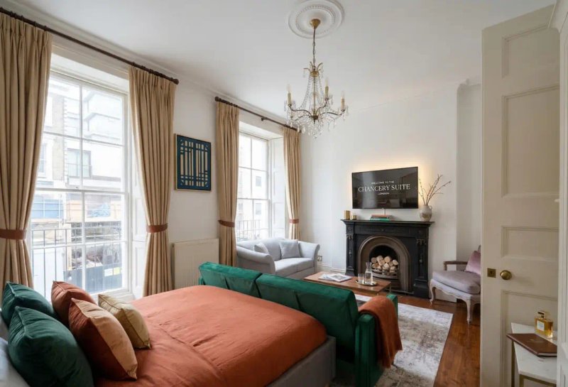 Bright bedroom with green sofa, coral bedding, fireplace and large windows with curtains.