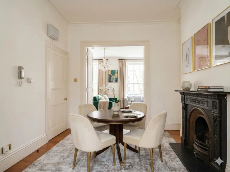 Dining area with round dark table, cream chairs, fireplace and window with natural light
