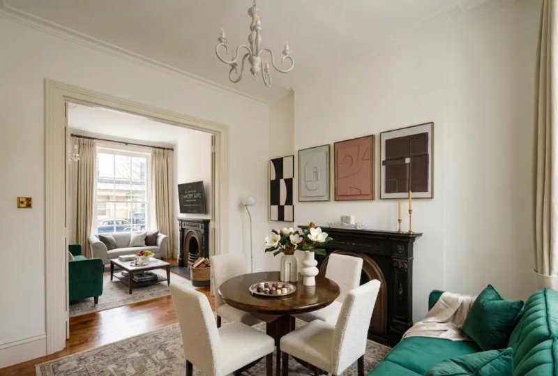 Elegant living room with fireplace, round dining table, cream chairs, and green sofa